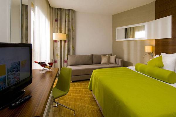 Innenansicht eines Hotelzimmers im Blue Waters Club mit Bett, Sofa, Fernseher und Schreibtisch.