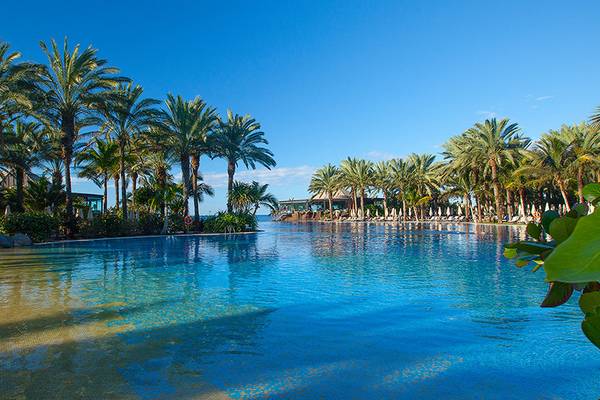 Ein großer Swimmingpool des Lopesan Costa Meloneras Resorts, umgeben von Palmen und Loungeliegen.