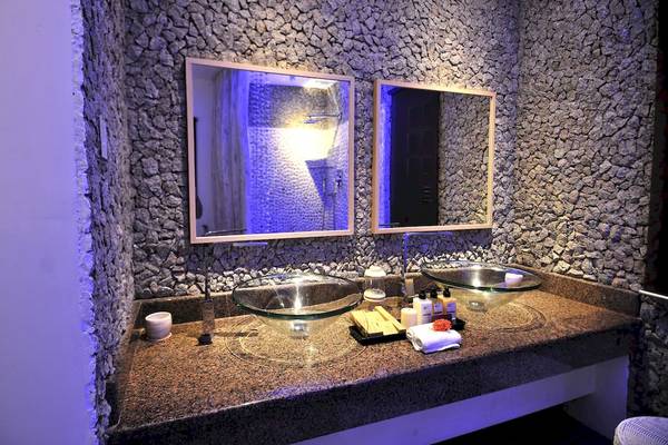 Badezimmer im Le Domaine de L'Orangeraie Resort & Spa mit Steinwand und zwei Waschbecken.