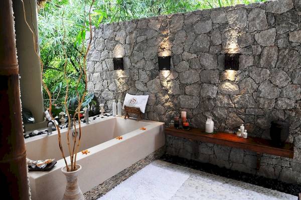 Luxuriöses Badezimmer mit Steinwand, Freiluft-Badewanne und Blick auf die Natur.