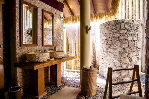 Innenbereich der Dusche im Le Domaine de L'Orangeraie Resort & Spa mit Steinwand, zwei Waschbecken und Holzmöbeln.