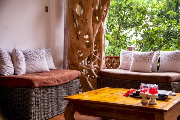 Innenbereich des Le Domaine de L'Orangeraie Resort & Spa mit zwei gepolsterten Bänken, Kissen, Tisch und Bäumen im Hintergrund.