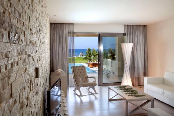 Innenansicht einer Hotelsuite mit Meerblick, einem Sofa, einem Tisch und einem Fernseher.