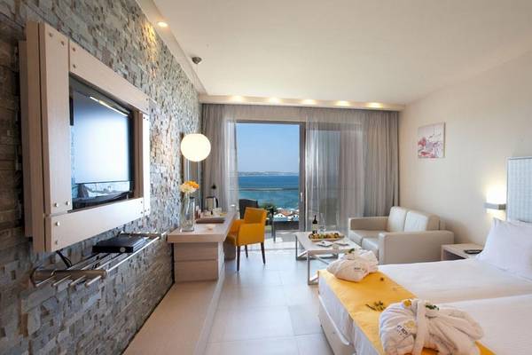 Innenansicht eines Hotelzimmers mit Meerblick, modern eingerichtet mit einem Fernseher, einem Schreibtisch, einem Sessel, einem Sofa, einem Tisch und einem Bett.