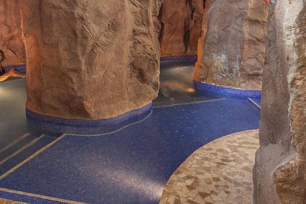 Eine Frau sitzt in einem blauen Wasserbecken, das von Felswänden umgeben ist, im Lopesan Costa Meloneras Resort & Spa.