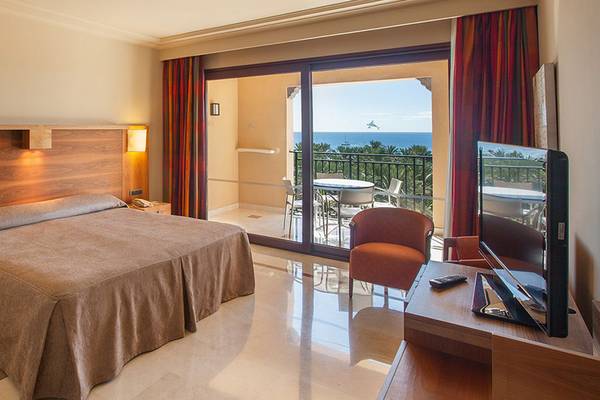 Hotelzimmer mit Meerblick im Lopesan Costa Meloneras Resort & Spa, mit Bett, Fernseher und Balkon mit Tisch und Stühlen.