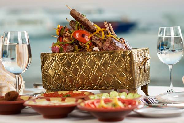 Luxuriöses Essen im Continental Hotel Hurghada mit gegrilltem Fleisch und Gemüse in einer goldenen Schale, serviert mit Wein und Beilagen.