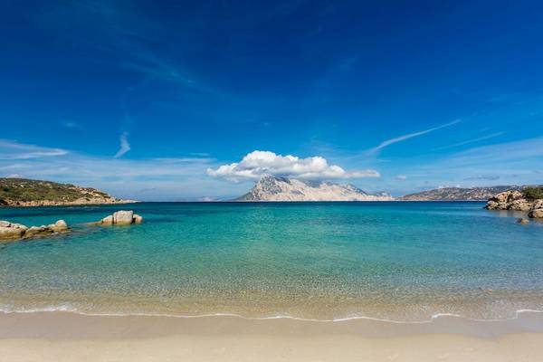 Strand mit klarem Wasser und Felsen am Horizont
