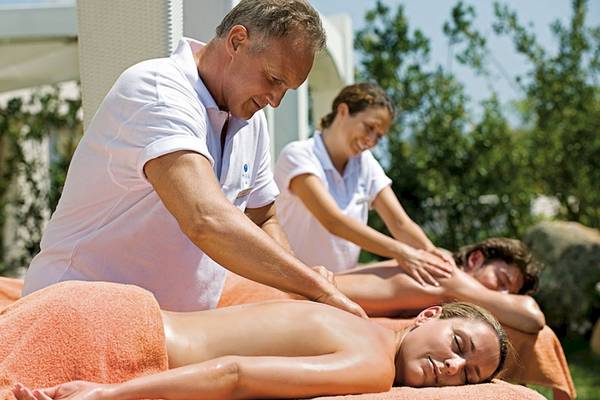 Massage im Grande Baia Resort & Spa mit drei Personen, eine Frau liegt entspannt auf einer orange Decke.