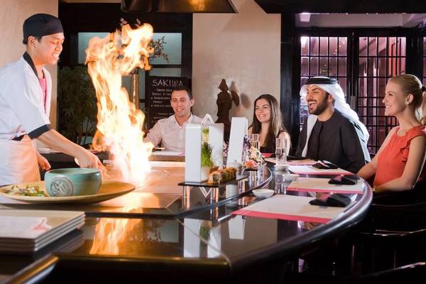 Gäste sitzen an einem Tisch im Millennium Plaza Downtown Sushi Bar und beobachten den Koch, der ein Gericht mit Feuer zubereitet.