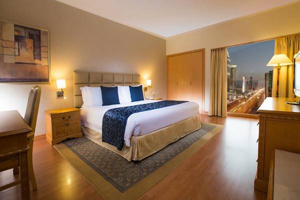 Schlafzimmer im Millennium Plaza Downtown Hotel mit großem Bett, Nachttischen und Stadtblick.