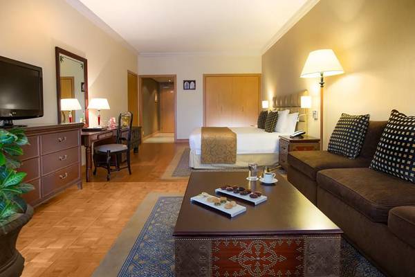 Innenansicht einer Hotelsuite im Millennium Plaza Downtown mit Bett, Wohnzimmer und Schreibtisch.