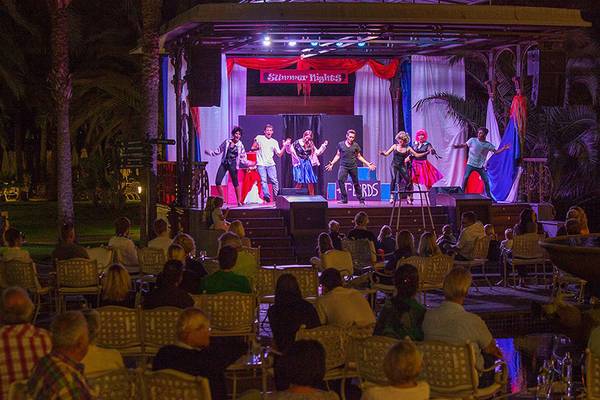 Eine Gruppe von Künstlern führt eine Show auf der Bühne des Lopesan Costa Meloneras Resorts & Spa auf, während das Publikum zuschaut.