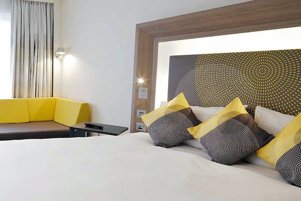 Ein stilvolles Zimmer im Novotel London Blackfriars mit einem Bett, gelben Kissen und einer modernen Kopfteilwand.