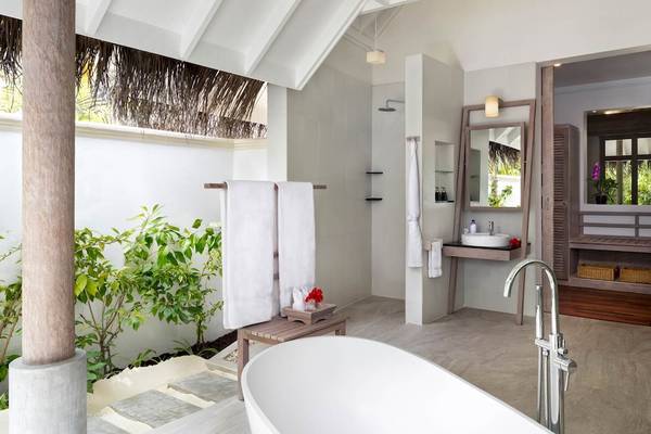 Innenansicht des Badezimmers im Anantara Dhigu Maldives Resort mit Badewanne, Dusche, Waschbecken und Pflanzen.