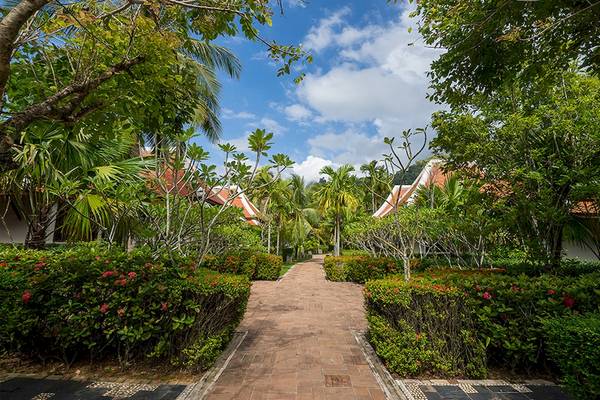 Gartenweg des Khao Lak Laguna Resorts mit roten Ziegelsteinen, umgeben von grünen Büschen und Bäumen.