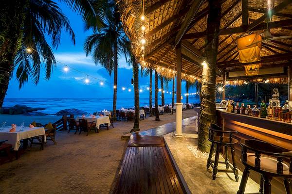 Abendansicht der Strandbar des Khao Lak Laguna Resorts mit beleuchteten Tischen und Stühlen.