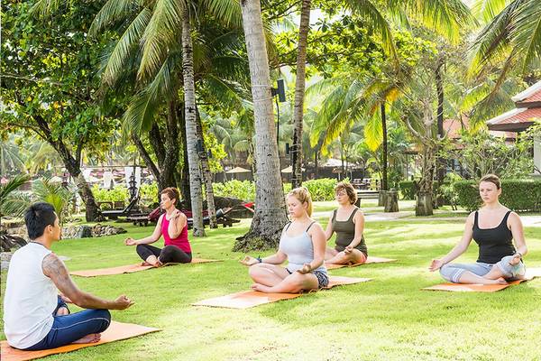 Ein Yogakurs im Freien im Khao Lak Laguna Resort mit fünf Teilnehmern, die auf Matten sitzen und meditieren.