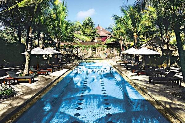 Ein Swimmingpool im Novotel Bali Benoa Hotel, umgeben von Palmen und Sonnenliegen.