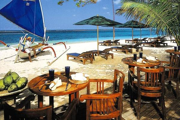 Novotel Bali Benoa Strand mit Sonnenliegen und Sonnenschirmen, mit einem Mann auf einem Segelboot.
