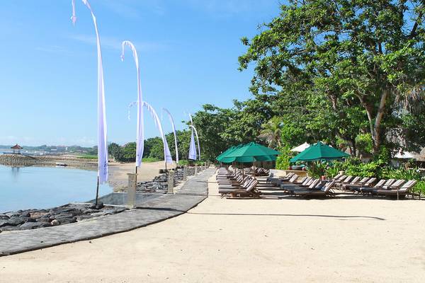 Novotel Bali Benoas Strand mit Sonnenliegen und grünen Sonnenschirmen.