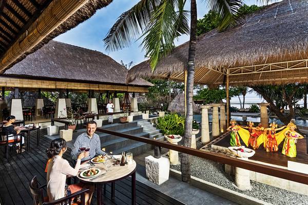 Paar im Novotel Bali Benoa, das draußen essen genießt, während sich Tänzer auf der Bühne vorbereiten.