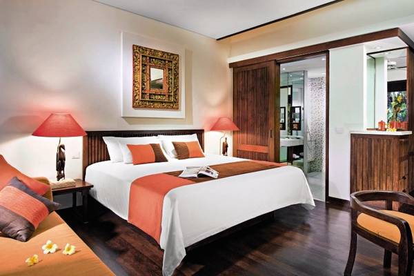 Innenansicht eines Zimmers im Novotel Bali Benoa mit einem Bett, Lampen, einem Tisch, Kissen und einem Holzboden.