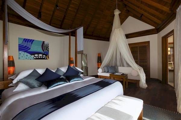 Schlafzimmer im Anantara Dhigu Maldives Resort mit großem Bett, Moskitoschurz und Sofa.