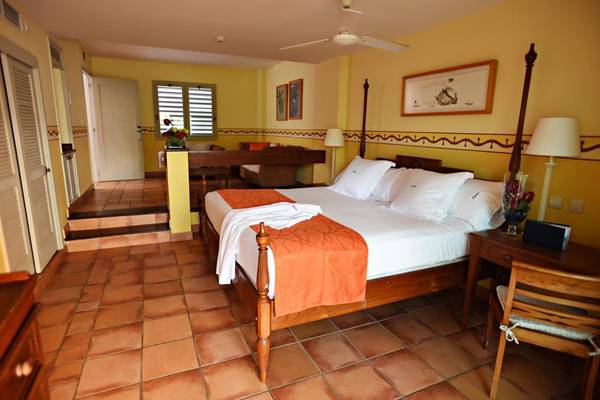 Schlafzimmer im Melia Varadero Hotel mit Doppelbett, gelben Wänden und Holzmöbeln.