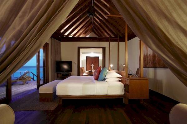 Schlafzimmer im Anantara Dhigu Maldives Resort mit Bett, Fernseher und Meerblick.