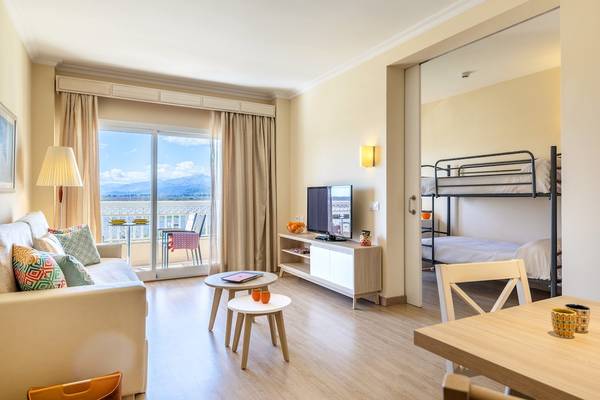 Wohnzimmer des Viva Blue & Spa Hotels mit Schlafsofa, Tisch, Fernseher und Balkon.