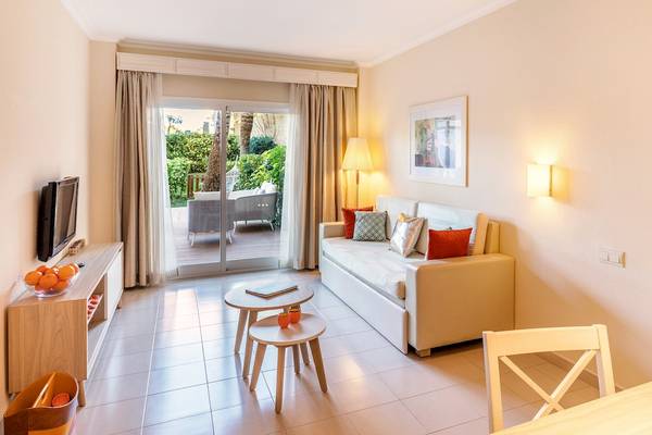Wohnbereich des Viva Blue & Spa Hotels mit Sofa, Fernseher und Glastür zum Balkon