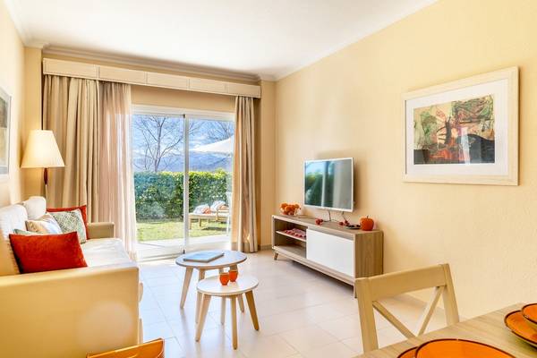 Wohnzimmer im VIVA Blue & Spa Hotel mit Couch, Tisch, Fernseher und Glastür zum Garten.
