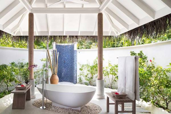 Ein Freiluft-Badezimmer im Anantara Dhigu Maldives Resort mit einer Badewanne, Pflanzen und einer überdachten Terrasse.