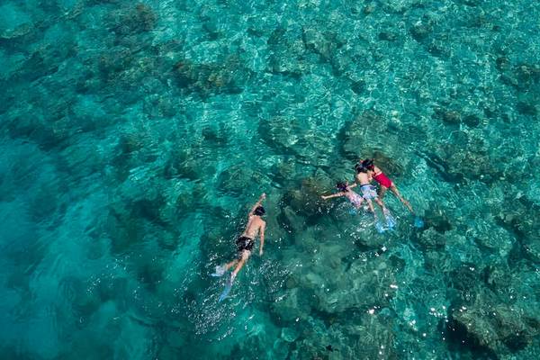 Drei Personen schnorcheln im kristallklaren Wasser vor dem Anantara Dhigu Maldives Resort.