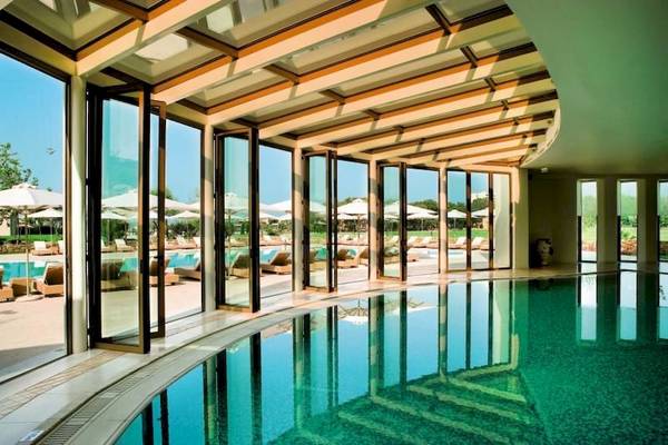 Innenpool des Porto Sani Hotels mit großen Glaswänden und Sonnenliegen draußen
