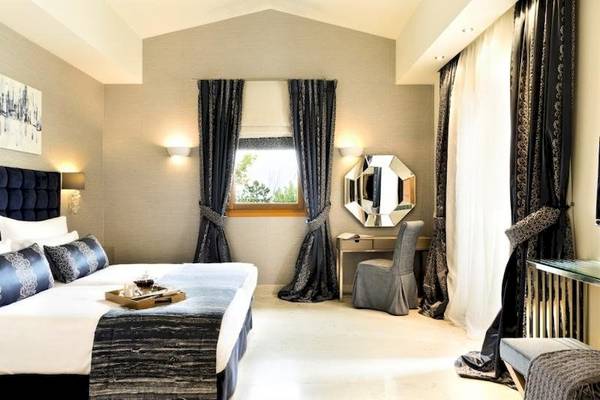 Ein elegantes Hotelzimmer im Porto Sani Hotel mit einem Bett, einem Schreibtisch und einem Spiegel.