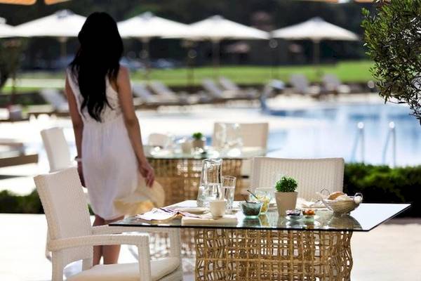 Frau im weißen Kleid steht am Frühstückstisch im Freien im Porto Sani Hotel