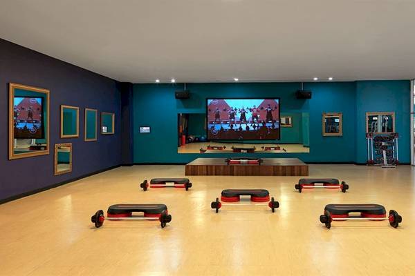 Fitnessraum im Hard Rock Hotel & Casino Punta Cana mit Trainingsgeräten und großen Bildschirm.