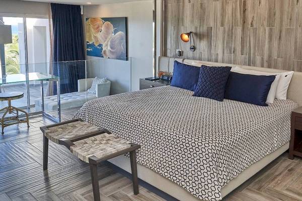 Schlafzimmer im Hard Rock Hotel & Casino Punta Cana mit großem Bett, blauen Kissen und hölzerne Wand.