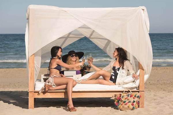 Drei Frauen sitzen auf einem Bett am Strand und trinken Getränke
