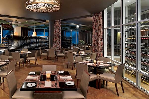 Restaurant-Innenbereich des Hard Rock Hotel & Casino Punta Cana mit runden Tischen, Stühlen und einer Bar im Hintergrund.