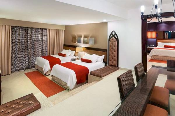 Innenansicht einer Suite im Hard Rock Hotel & Casino Punta Cana mit zwei Betten, einem Esstisch und Stühlen.