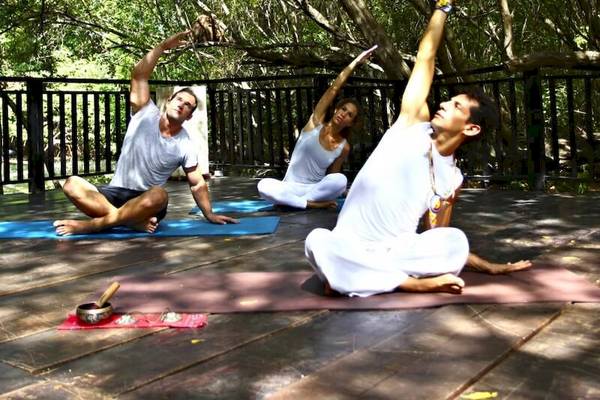 Drei Personen praktizieren Yoga auf einer Terrasse im Freien im Sandos Caracol Eco Resort.