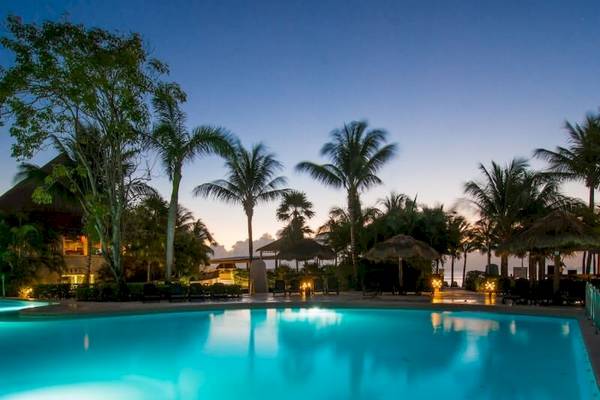 Pool im Sandos Caracol Eco Resort bei abendlicher Stimmung mit leuchtenden Lichtern und Palmen.