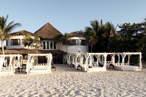 Das Sandos Caracol Eco Resort mit weißen Loungebetten am Strand und einer architektonischen Struktur im Hintergrund.