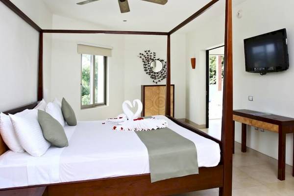 Schlafzimmer im Sandos Caracol Eco Resort Hotel mit Himmelbett, Fernseher und Dekoration.
