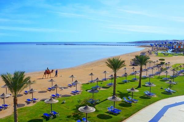 Luftaufnahme des Jaz Aquamarine Resorts mit Strand, Palmen, Sonnenliegen und einem Kamelritt.