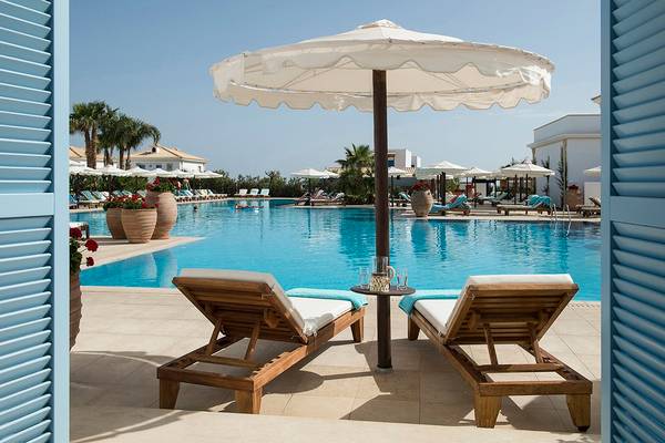 Außenbereich des Mitsis Laguna Resorts mit Swimmingpool, Sonnenliegen und Sonnenschirm.