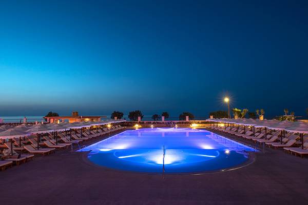 Beleuchteter Swimmingpool des Mitsis Laguna Resorts bei Nacht mit Sonnenliegen und Schirmen